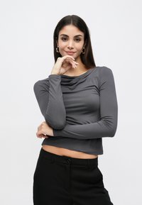 Γκρι τοπ με μακριά μανίκια και ντραπέ λαιμόκοψη, με απαλό ύφασμα και εφαρμοστή σχεδίαση, συνδυασμένο με μαύρο παντελόνι με κούμπωμα με κουμπιά.