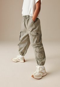 Helle grüne Cargo-Hosen mit elastischem Bund, seitlichen Taschen und schmal zulaufenden Bündchen, kombiniert mit weißen Sportschuhen und sichtbaren weißen Socken.