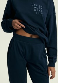 Granatowy sweatshirt z białym napisem "DREAM. PLAN. HAVE FUN." w zestawie z pasującymi spodniami dresowymi z bocznymi kieszeniami i ściągaczami przy nogawkach.