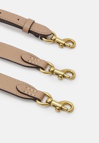 Kitched leather straps menonjolkan perangkat keras berwarna emas dengan klip berputar, detail jahitan, dan tekstur halus, ditempatkan dalam perataan paralel.