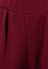 Gros plan d'un tissu rouge foncé avec un pli profond et une texture lisse, montrant une partie du design structuré d'un vêtement.