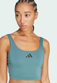 Teal sport crop top gemaakt van gladde stof, met een brede ronde hals en een zwart adidas-logo op de voorkant.