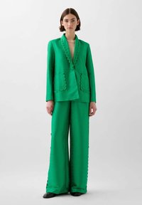 Green tailored suit featuring a blazer with scalloped edges and matching wide-leg trousers, both in a textured fabric.