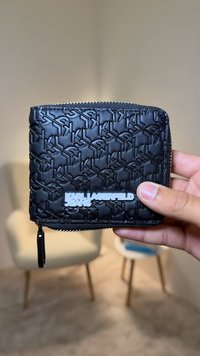 Black wallet made of textured material, featuring a repeating logo pattern. Front displays "KARL LAGERFELD JEANS" in white lettering. Zipper closure.