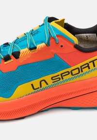 Baskets de sport avec une tige en maille bleue, orange et jaune. Présentent des accents noirs, des superpositions texturées et un logo bien visible sur le côté.