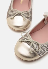Bailarinas con puntera metálica dorada y parte superior de tejido plateado texturizado, con un detalle de lazo a juego y plantilla rosa.