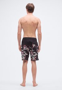 Čierne plavecké šortky s kvetinovým vzorom v ružovej a zelenej farbe, s hladkým pásom a voľným strihom. Sú viditeľné švy a sú pridané vrecká.