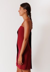 Abito bordeaux con spalline sottili, caratterizzato da un corpino aderente e una parte posteriore ampia. Il tessuto morbido e l'orlo a lunghezza ginocchio creano una silhouette elegante.