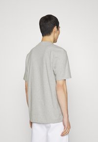 Camiseta de manga corta gris claro con escote de cuello redondo, hecha de tela suave, presenta un ajuste relajado y un diseño minimalista. Vista trasera mostrada.