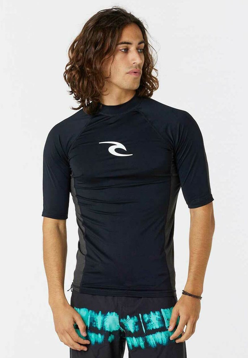 Sort kortærmet rash guard med et hvidt logo på brystet; slank design og tætsiddende silhuet, parret med mørke shorts med turkis detaljer.