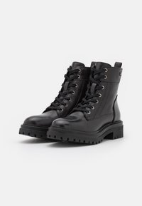 Botas de cuero negro hasta el tobillo con punta redonda, que cuentan con ojales metálicos, cordones y una gruesa suela de goma negra con un patrón de dibujo.