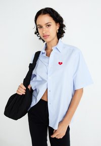 Light blue short-sleeve button-up shirt with white stripes and a red heart-shaped embroidery on the left chest. Worn with black pants.