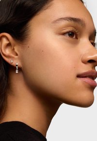 I orecchini a cerchio in argento presentano un accento nero e tre perline in argento, mettendo in mostra un design elegante. Lo sfondo è di un colore chiaro e uniforme.