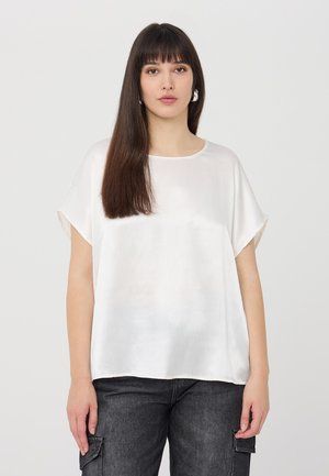 Top corto bianco in satin con scollatura tonda, vestibilità rilassata, con maniche arrotolate e una texture liscia, abbinato a pantaloni cargo scuri.