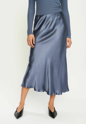 Satin midi seelik sügavas mereväes, sujuva tekstuuri ja laieneva alumise servaga. Kõrvale sobitatud kitsas pikkade varrukatega topp ja mustad teravadega baleriinad.