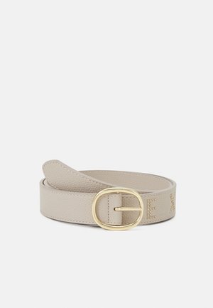 Ceinture en cuir beige texturé avec une boucle ovale en or et des lettres cloutées partiellement visibles sur un fond uni.