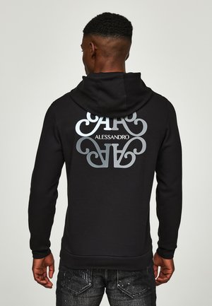 Homme portant un sweat à capuche noir avec des lettres miroirs stylisées et le texte "ALESSANDRO" dans le dos, associé à un jean foncé.