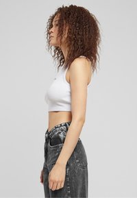 Hvit ribbet crop topp med ermeløs design, parret med høytsittende svarte denimjeans med falmet tekstur og knappelukking.