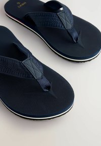 Navy blue flip-flops with textured fabric straps, rubber soles featuring a white trim, and a simple design with a wide toe post.