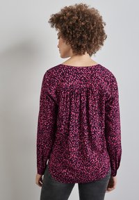 Långärmad blus i livlig rosa med mörka abstrakta mönster, med en avslappnad passform, rundad halsringning och draperingsdetalj längs ryggen.