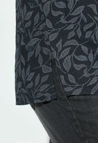 Donkerblauwe blouse met grijs bladpatroon, lichtgewicht textuurstof, zijsplit, gecombineerd met donkere jeans, met zichtbare zoomdetails.