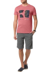 Růžové bavlněné tričko s krátkým rukávem a modro-černým grafickým potiskem, spárované s šedými šortkami a námořnickými slip-on botami.