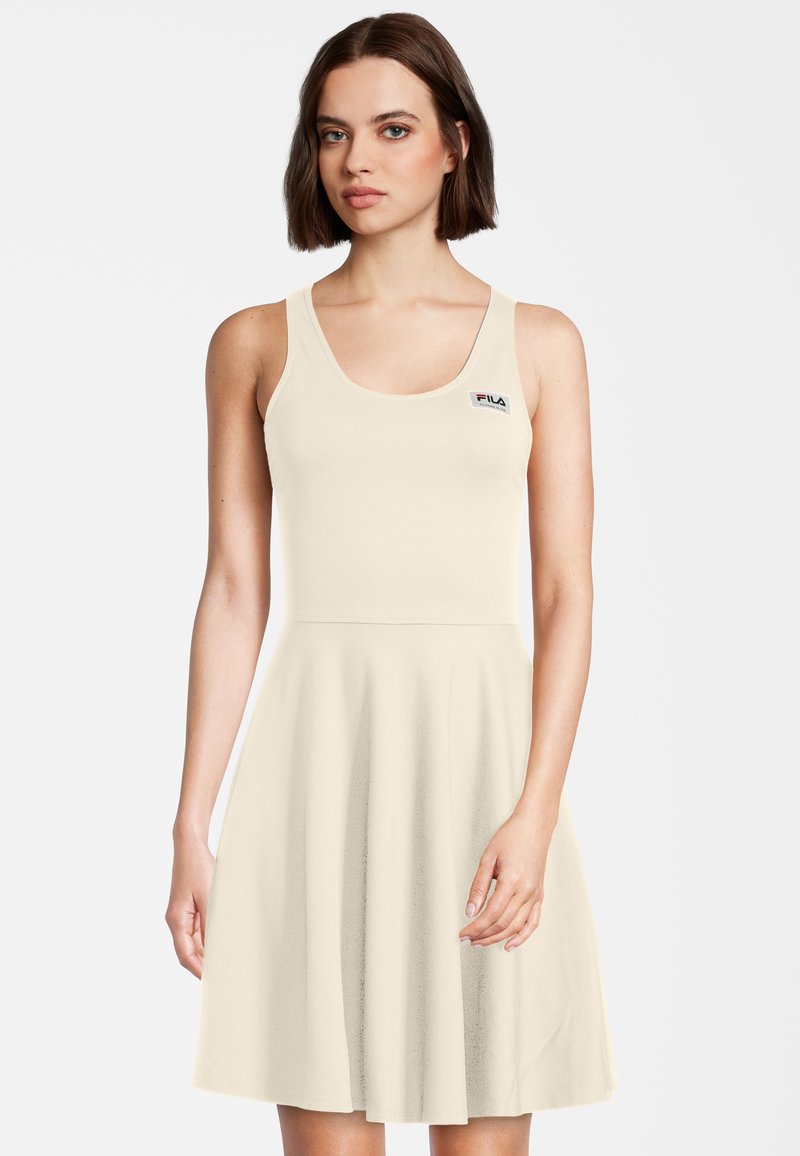 Tan kleurige mouwenloze jurk met een aansluitende top en een uitlopende rok, gemaakt van zachte stof. Heeft een klein FILA-logo op de borst.