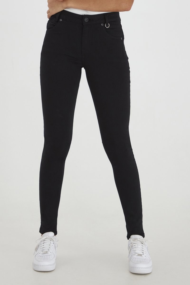 Fekete, slim fit szabású, skinny farmernadrág, elöl gombos záródással, zsebekkel és övhurkokkal, fehér sportcipővel párosítva.