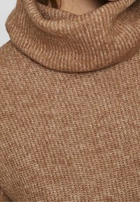 Maglione marrone lavorato a maglia con un alto colletto a coste e un motivo fine e texturizzato su tutta la superficie. Il materiale sembra morbido e caldo.