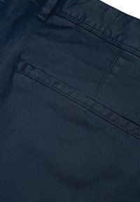 Marineblaue Hose mit glattem Stoff, klassischem Design und einer hinteren Tasche mit sauber genähter Kante. Texturierte Oberfläche sichtbar.