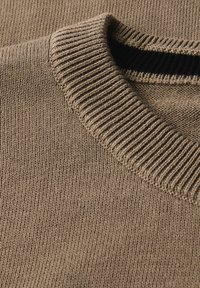 Brun stickad tröja med en ribbad rundhalsringning och en slät textur, med en kontrasterande mörk inre halsringning.