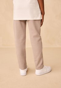 Pantalon de survêtement beige clair en matériau doux, avec une coupe droite et une taille élastique, associé à des baskets blanches.