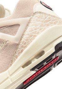 Κοντινή λήψη της σόλας αθλητικού παπουτσιού σε μπεζ και εκρού χρώμα, με υφή στη πλευρική επιφάνεια, ορατό αερόσακο και μέρος της μαύρης και κόκκινης εξωτερικής σόλας.