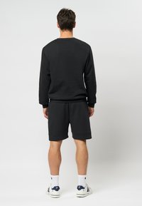 Hanorac negru cu guler clasic și mâneci lungi, asortat cu pantaloni scurți negri. Materialul pare moale, având manșete și tiv dublat.