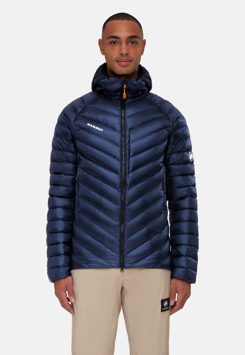 Marineblauwe geïsoleerde jas met een chevron-quiltpatroon, hoge kraag en een ritssluiting aan de voorkant met een oranje trekband, gemaakt van lichtgewicht materiaal.