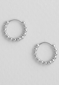 Silberne Creolen mit einem kreisförmigen Design und gleichmäßig verteilten kugelförmigen Akzenten. Glatte, polierte Metalloberfläche mit glänzendem Finish.