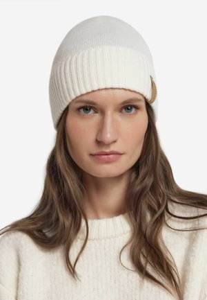 Witte gebreide muts met geribbelde textuur en een omgeplooide boord. Voorzien van een kleine ronde beige accent aan de zijkant. Zachte, warme stof.