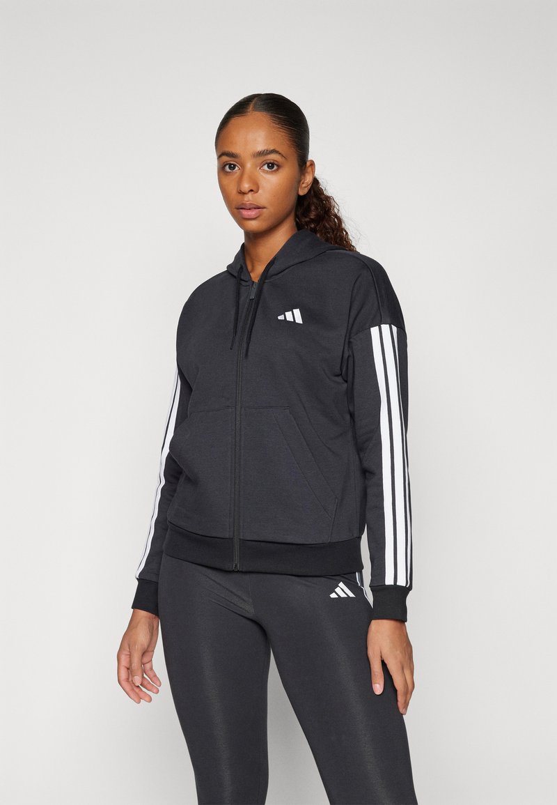 Black zip-up hoodie with a hood. Features white three-stripe accents on sleeves and Adidas logo on the chest. Made from soft, textured fabric.