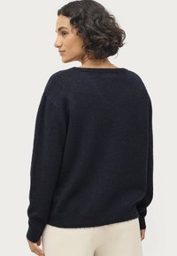 Marineblauer Strickpullover mit lockerer Passform, langen Ärmeln und geripptem Halsauschnitt, der eine weiche Textur und dezente Farbvariationen aufweist.