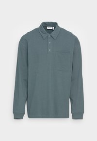 Long-sleeve polo shirt in slate blue cotton, featuring a classic collar, two snaps, and a chest pocket with a single stitching detail.