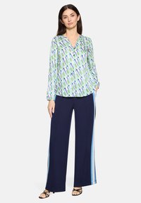 Leichte, gemusterte Bluse in Grün- und Blautönen mit V-Ausschnitt und Knopfdetails, kombiniert mit marineblauen, weit geschnittenen Hosen mit seitlichen Streifen.