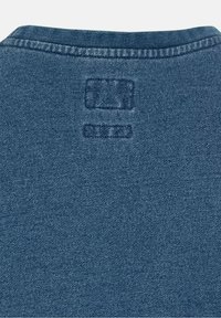 Tessuto denim di un blu intenso con una superficie testurizzata. Presenta un'etichetta stampata sul colletto, che arricchisce la semplicità del design.