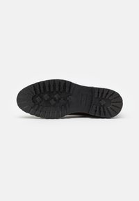 Suela de zapato de goma negra con profundas estrías y patrones en cruz; presenta una etiqueta rectangular con la talla "42" estampada en el lateral.