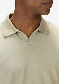 Pikétröja i ljusgrön tyg, med en krage som har en kontrasterande beige kant och en V-halsdesign. Slät yta, inga mönster.