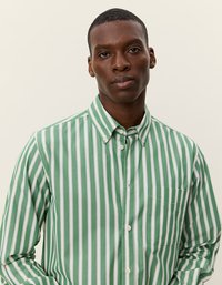 Zaļi un balti svītrota pogājamā krekla ar apkakli, kreisā krūts kabata un gluda kokvilnas auduma. Vertikālas svītras, parastā piegriezuma.