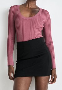 Helles rosa, geripptes Langarmoberteil mit rundem Ausschnitt, kombiniert mit einem figurbetonten schwarzen Minirock, der glatte Texturen und kontrastierende Farben präsentiert.