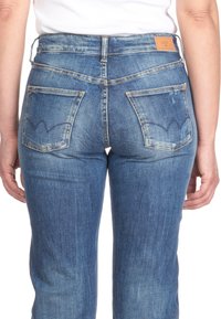 Denim jeans in a medium blue wash with a subtle faded pattern, featuring two back pockets and a leather brand tag on the waistband.