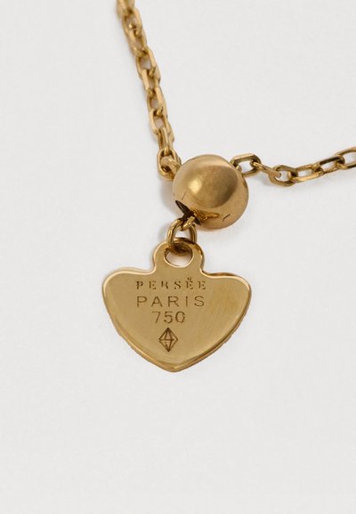 Goldkette mit einem herzförmigen Anhänger. Der Anhänger ist mit dem geprägten Text "PERSÉE PARIS 750" und einer runden Metallperle versehen.