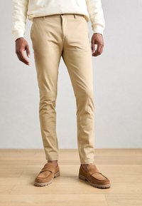 Beige katoen-chino broeken met een slim fit, voorzien van riemlussen en een knoopsluiting, gecombineerd met tan suède instappers.