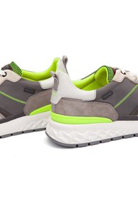 Zapatillas gris y beige con un acabado de ante texturizado, detalles en verde y un interior de malla con patrón. Cuenta con una suela acolchada.